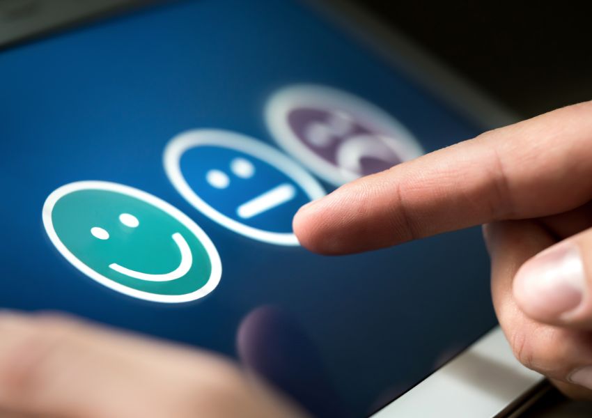 A hand presses a neutral face icon on a digital satisfaction rating scale displayed on a touchscreen device.