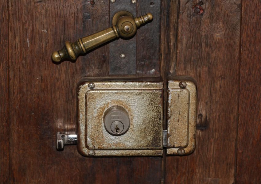 Close-up of an old wooden door with a worn metal lock and latch, symbolising traditional physical security.